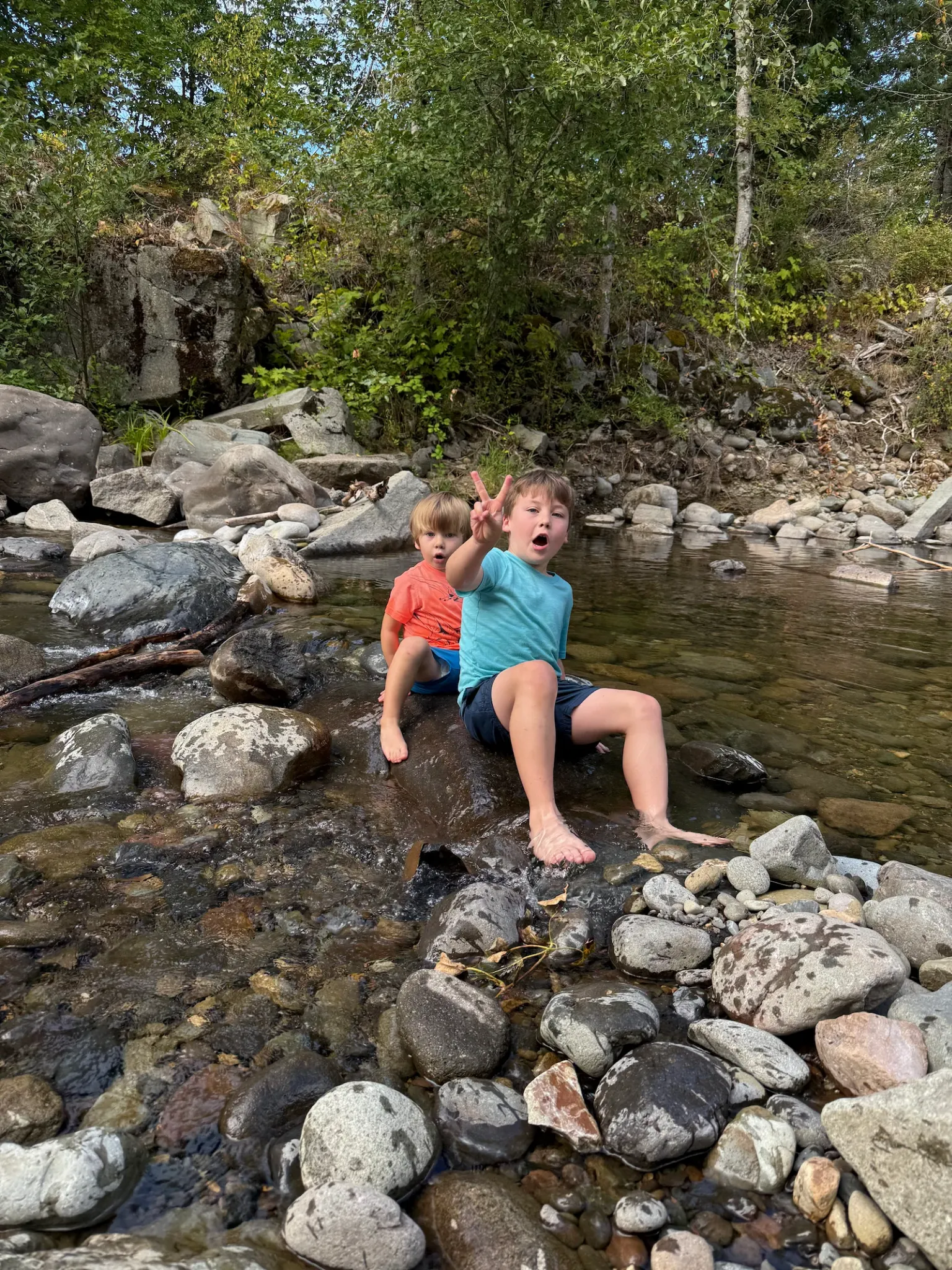 Two children sitting on rocks in the shallow river during a family outing